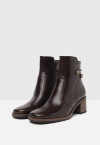 Bottines en cuir marron avec une fermeture éclair sur le côté, un talon empilé et des détails en métal. Texture lisse et design élégant.