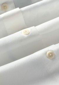 Gros plan d’un tissu blanc avec trois boutons couleur crème alignés cousus sur les bords pliés du tissu.