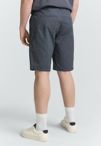 Graue strukturierte Shorts mit geradem Schnitt, seitlichen und hinteren Taschen sowie umgeschlagenen Säumen, kombiniert mit weißen Socken und cremefarbenen Turnschuhen.