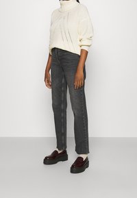 Weißer, gestrickter Rollkragenpullover, schwarze Jeans mit geradem Bein und burgunderrote Plateau-Pumps aus Lackleder. Strukturierter Stoff und lässige Passform.