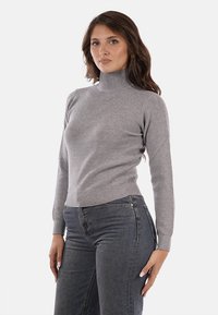 Maglione a collo alto grigio chiaro realizzato in tessuto a costine, design aderente, maniche lunghe, collo alto e polsini a costine, abbinato a jeans di denim scuro.
