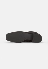 Semelle de chaussure noire avec une surface lisse et texturée, dotée d'un talon plat et d'un design légèrement profilé. Pas de marque visible.