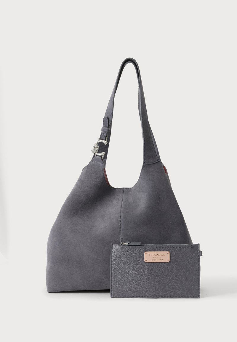 Sac à main en daim gris foncé avec une large bandoulière et une fermeture argentée, accompagné d'un portefeuille zippé en cuir gris foncé assorti avec une étiquette de marque beige.