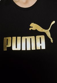 Black t-shirt featuring bold, shiny gold "PUMA" text and logo. Material appears smooth with a simple, classic crew neck design.