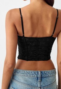 Mustat lyhythihaiset paita, joka on valmistettu pintakuvioidusta pitsistä. Siinä on ohuet säädettävät olkaimet ja rakenteellinen istuvuus, jossa on saumat takana.