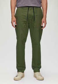 Pantalons légers verts avec taille à cordelette, poches latérales et coupe droite, associés à des baskets beiges.
