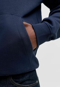 Navy sweatshirt with ribbed cuffs and a kangaroo pocket. Fabric appears soft with a smooth texture. Visible stitching detail near the hem.