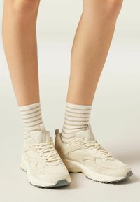 Beżowe buty sportowe z teksturowanej siateczki i zamszowymi akcentami, z sznurowadłami, pętelką do zakładania i szarym gumowym podnoskiem. W zestawie ze skarpetkami w paski.