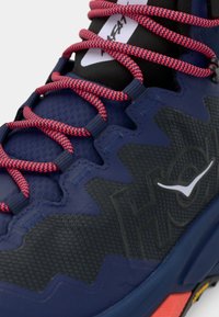 Μπλε αθλητικό παπούτσι με υφασμένο επάνω μέρος, κόκκινα και μαύρα κορδόνια με σχέδιο και διαμορφωμένη σόλα με πορτοκαλί και μαύρες λεπτομέρειες.