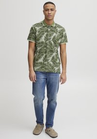 Zöld, rövidujjú poloing pálmalevél mintázattal, kék farmernadrággal és bézs slip-on cipővel párosítva. Slim fit fazon, gallérral.
