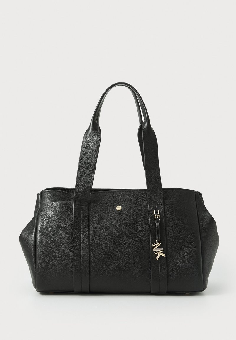 Sac à main en cuir noir texturé avec double bandoulière et un pendentif métallique avec le logo MK sur une bandoulière, sur un fond clair uni.