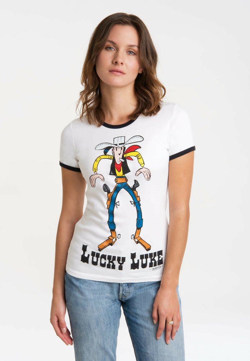 Weißes Baumwoll-T-Shirt mit buntem "Lucky Luke"-Motiv, runder Ausschnitt und schwarzem Besatz an den Ärmeln. Hellblaue Jeans.