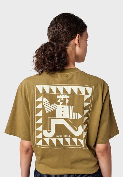 Olivově zelené bavlněné oversized tričko s velkým bílým potiskem na zádech, znázorňující hravou postavu s geometrickými vzory.