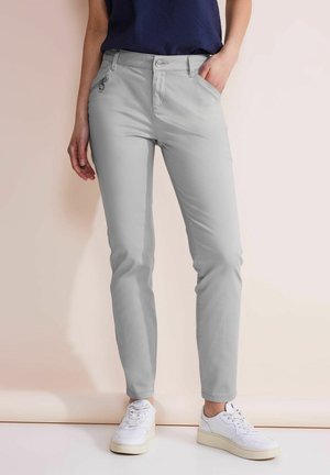 Pantalons slim gris clair avec une texture lisse, fermeture éclair et bouton, et deux poches avant. Associés à des baskets blanches.