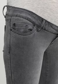 Jeans de denim gris con un ajuste slim, que cuentan con un bolsillo frontal, costuras visibles y una cintura de altura media con una sutil textura.