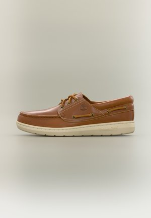 Chaussure bateau Timberland en cuir marron avec laçage à l’avant et semelle blanche en caoutchouc, vue de profil sur un fond neutre.