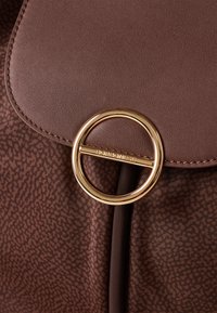 Brown textured handbag with a smooth leather flap. Features a gold circular hardware accent and tonal stitching. Patterned fabric base.