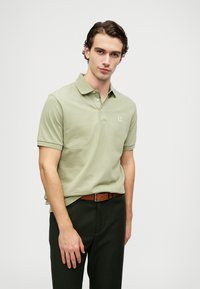 Polo de manga curta em algodão verde claro, com colarinho, pala de dois botões e um pequeno logótipo bordado no peito.