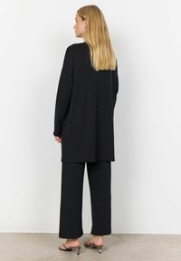Zwarte oversized sweatshirt en bijpassende wijde broek. Zachte stof met een gladde textuur, voorzien van een minimalistisch ontwerp. Geaccentueerd met bedrukte schoenen.