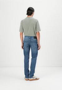 T-shirt vert clair, jeans en denim bleu, coupe décontractée, vue de derrière. Les jeans présentent une pièce à la taille et des poches standard, la texture du tissu est lisse.