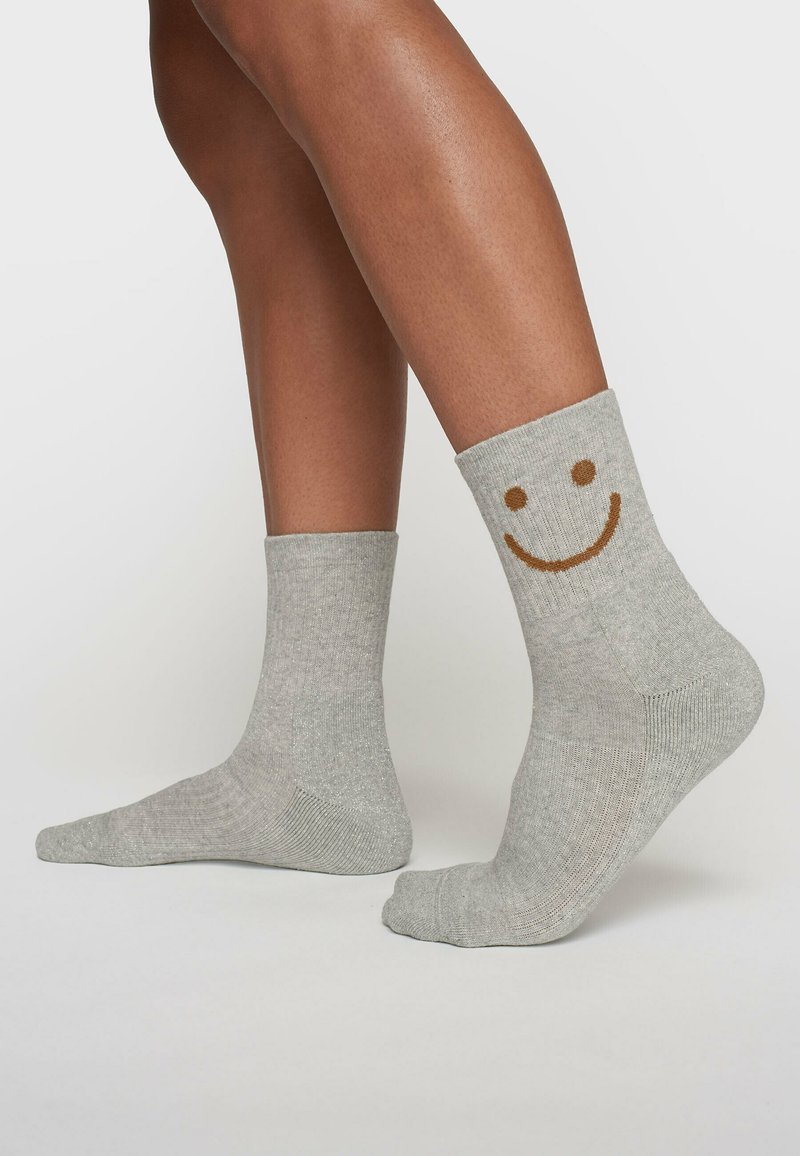 Szare bawełniane skarpetki z prążkowanymi mankietami, ozdobione brązowym wzorem uśmiechniętej buźki. Krótkie, do kostek, o gładkiej teksturze i wzmocnionym palcu.