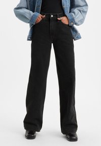 Črne široke kavbojke iz jeansa z visokim pasom, velikimi žepi in minimalističnim dizajnom. Združene s svetlomodro jeans jakno.