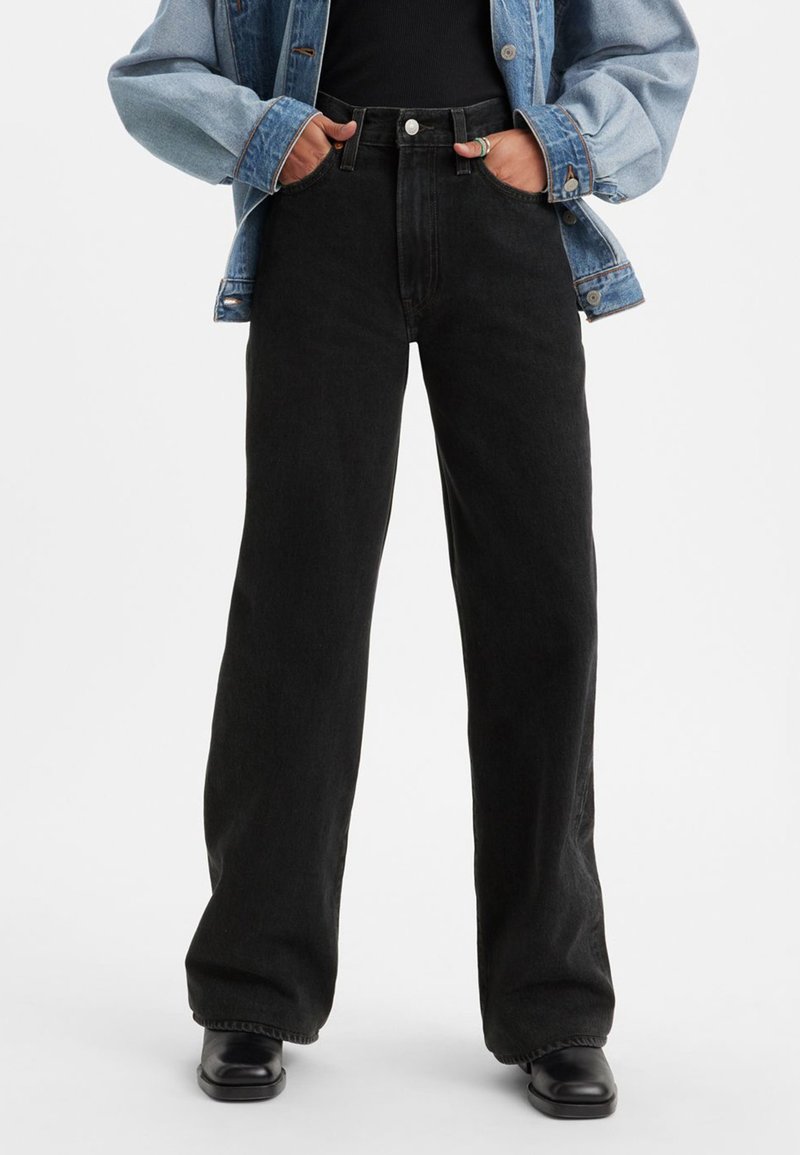 Črne široke kavbojke iz jeansa z visokim pasom, velikimi žepi in minimalističnim dizajnom. Združene s svetlomodro jeans jakno.