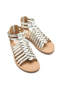 Sandales argentées à lanières avec un design tissé, présentant une semelle plate en cuir brun et une bride ajustable à la cheville pour un maintien sécurisé.