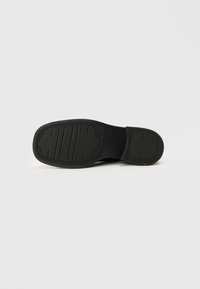 Μαύρη σόλα παπουτσιού από καουτσούκ με υφή λαβής, οβάλ σχήμα και στρογγυλεμένες άκρες. Διαθέτει επίπεδο σχέδιο για σταθερότητα και πρόσφυση.