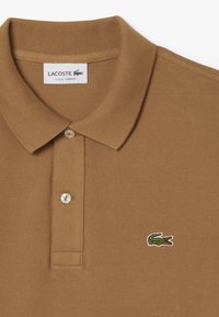 Brun polo skjorta i texturerad bomull, med ribbad krage, tvåknapps knäppning och en liten grön krokodil-logotyp på bröstet.