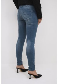 Mršavi plavi traperice s izblijedjelim pranjem, s stražnjim džepovima i strukom srednje visine, uparenim s crnim cipelama na visoku petu.