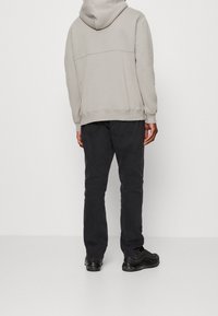 Hellgrauer Kapuzenpullover mit Kängurutasche, kombiniert mit dunklen schwarzen Hosen und schwarzen Sneakers. Auffälliger Strukturstoff und enganliegende Bündchen.