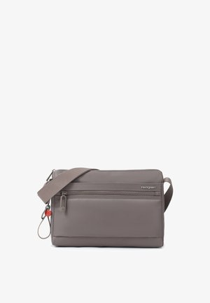 Petit sac bandoulière gris compact avec poche zippée à l'avant, bandoulière réglable et petit pendentif rouge sur anneau métallique.