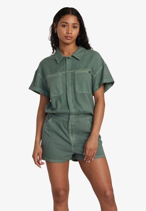 Green denim short jumpsuit with a collar, short sleeves, two front pockets, and a fitted waist. Features stitching details and a front button closure.