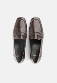 Καφέ λουστρίνι μοκασίνια με στρογγυλερή μύτη, ραμμένες λεπτομέρειες και λεία υφή. Διαθέτουν διπλή ραφή στην επάνω γραμμή και μαλακό πάτο.