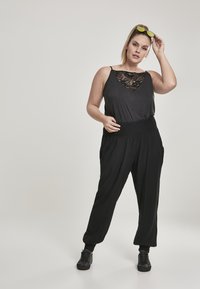 Top sans manches noir en tissu lisse avec un détail en dentelle au niveau du décolleté, associé à un pantalon noir ample avec une taille élastique.