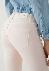 Jeans de color rosa claro con costuras blancas y un detalle en el bolsillo trasero. La etiqueta muestra la marca "LTB". Lleva puesta una chaqueta de mezclilla clara.