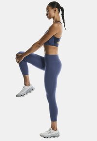 Marineblauer Sport-BH mit einem Ausschnitt-Design, kombiniert mit passender hoch taillierter Leggings. Weiße Laufschuhe mit dicken Sohlen.