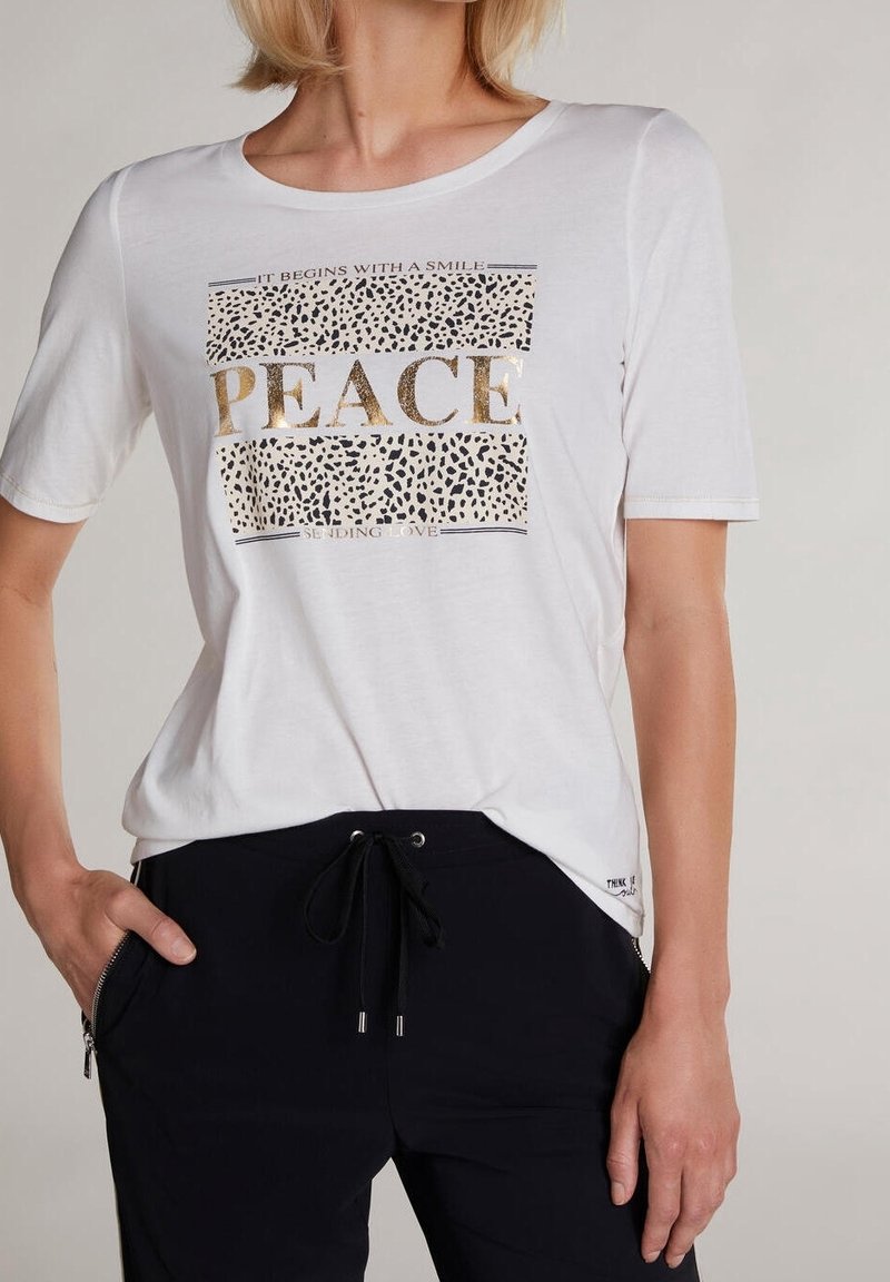 Wit T-shirt met korte mouwen, voorzien van een metalen gouden "PEACE"-tekst en accenten in dierenprint. Zachte stof met een losse pasvorm, gecombineerd met donkere broek.