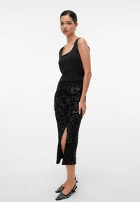 Crna majica bez rukava uparenjena s crnom suknjom oslikanom šljokicama koja ima visok prorez do bedra i slingback cipelama s crno-bijelim uzorkom.