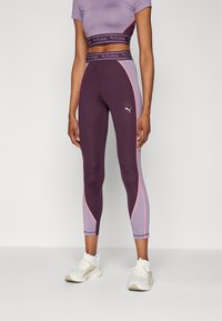 Sötétlila leggings világoslila és rózsaszín kiegészítőkkel, rugalmas anyagból készült. Egy megfelelő rövid fazonú toppal és fehér sportcipővel párosítva.