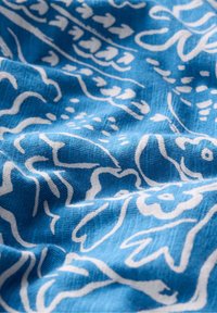Textile bleu avec un motif floral et abstrait blanc, présentant une finition douce et texturée, affichant de légères plis et rides.