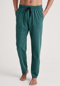 Groene, losse loungebroek met een elastische tailleband, aantrekkoord en zijzakken; gemaakt van zacht, gestuct materiaal.