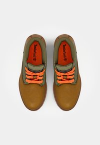 Chaussures en cuir marron avec des accents en textile vert, des lacets orange et une semelle intérieure rembourrée. Elles présentent un bout rond et un design de semelle robuste.