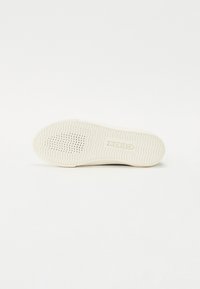 Sola de sapato de borracha branca com superfície texturizada, apresentando um padrão ondulado e furos de ventilação. Logótipo e nome da marca aparecem perto do calcanhar.