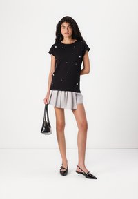 Black short-sleeve top with decorative silver dots, paired with a pleated gray mini skirt and black pointed-toe heels, complemented by a small bag.