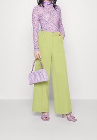 Světle fialový květinový rolák, kalhoty s vysokým pasem ve světlé zelené barvě a širokým střihem, levandulová kabelka a odpovídající pletené sandály.