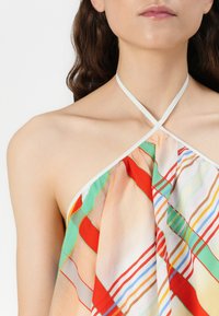 Haut halter coloré en tissu léger à carreaux avec des rayures rouges, vertes et oranges. Il a un nœud cou blanc et une texture douce.