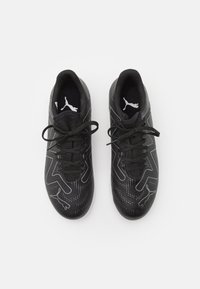 Scarpe da ginnastica nere con una parte superiore testurizzata, caratterizzate da design con contorni bianchi e loghi ricamati. I lacci sono neri e strettamente allacciati.