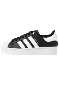 Mustat nahkakengät valkoisilla yksityiskohdilla, joissa on kolme valkoista raitaa, teksturoitu kumikärkiosa ja kultainen "Superstar"-merkintä.